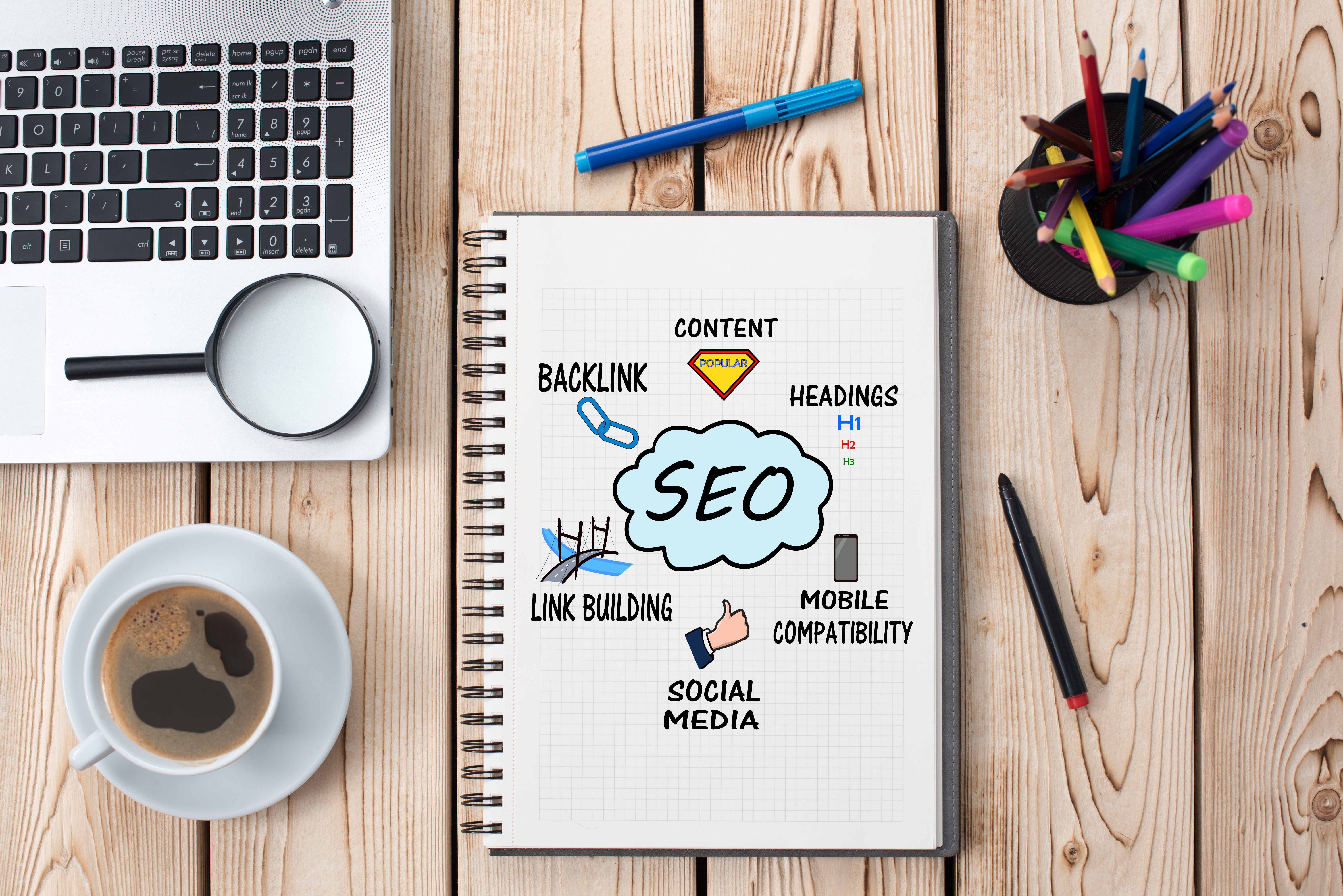 a top down image of a desk with stationery a laptop a cup of coffee and a book with SEO written on the page